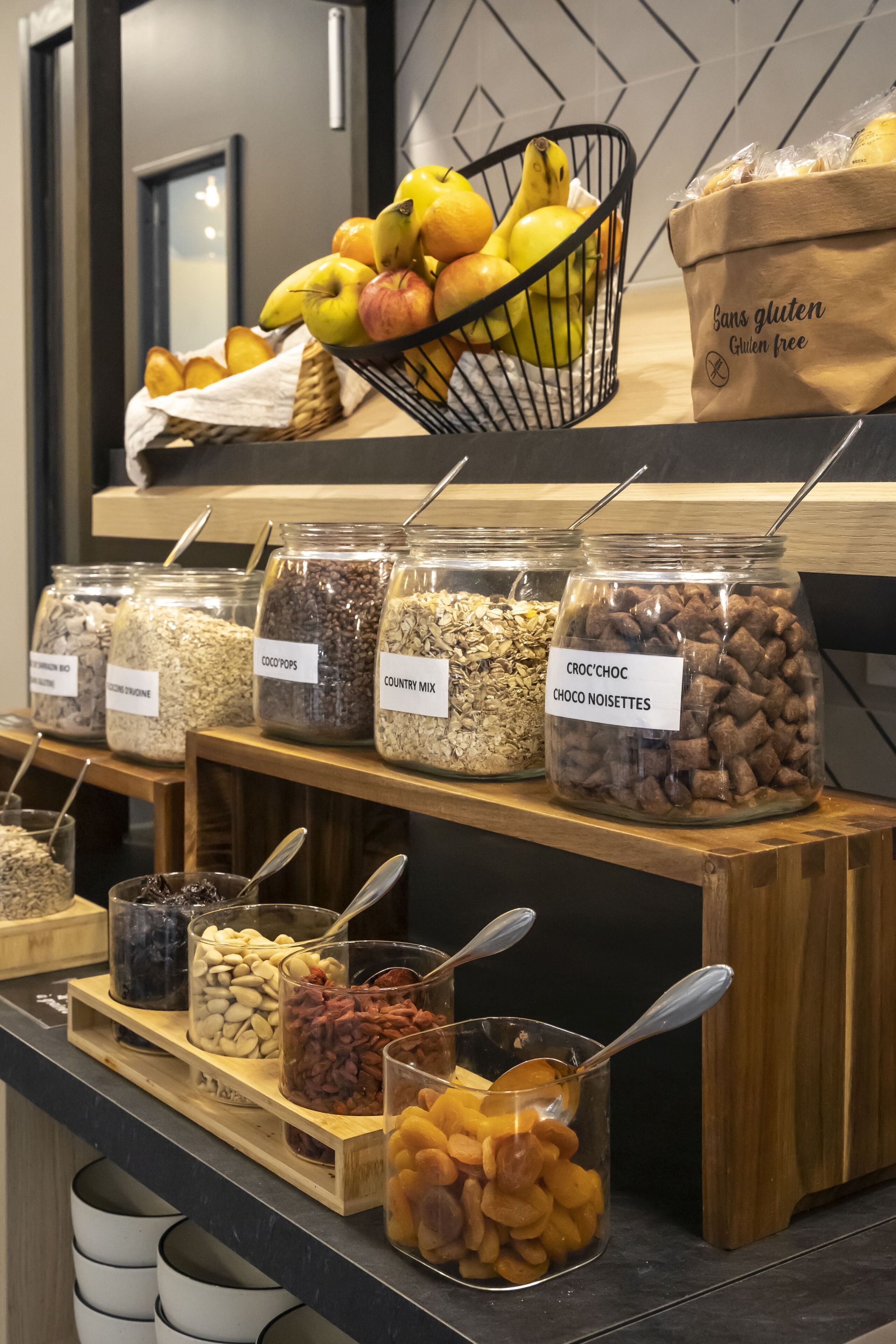 A food display with various jars of snacks and a basket of fruits.