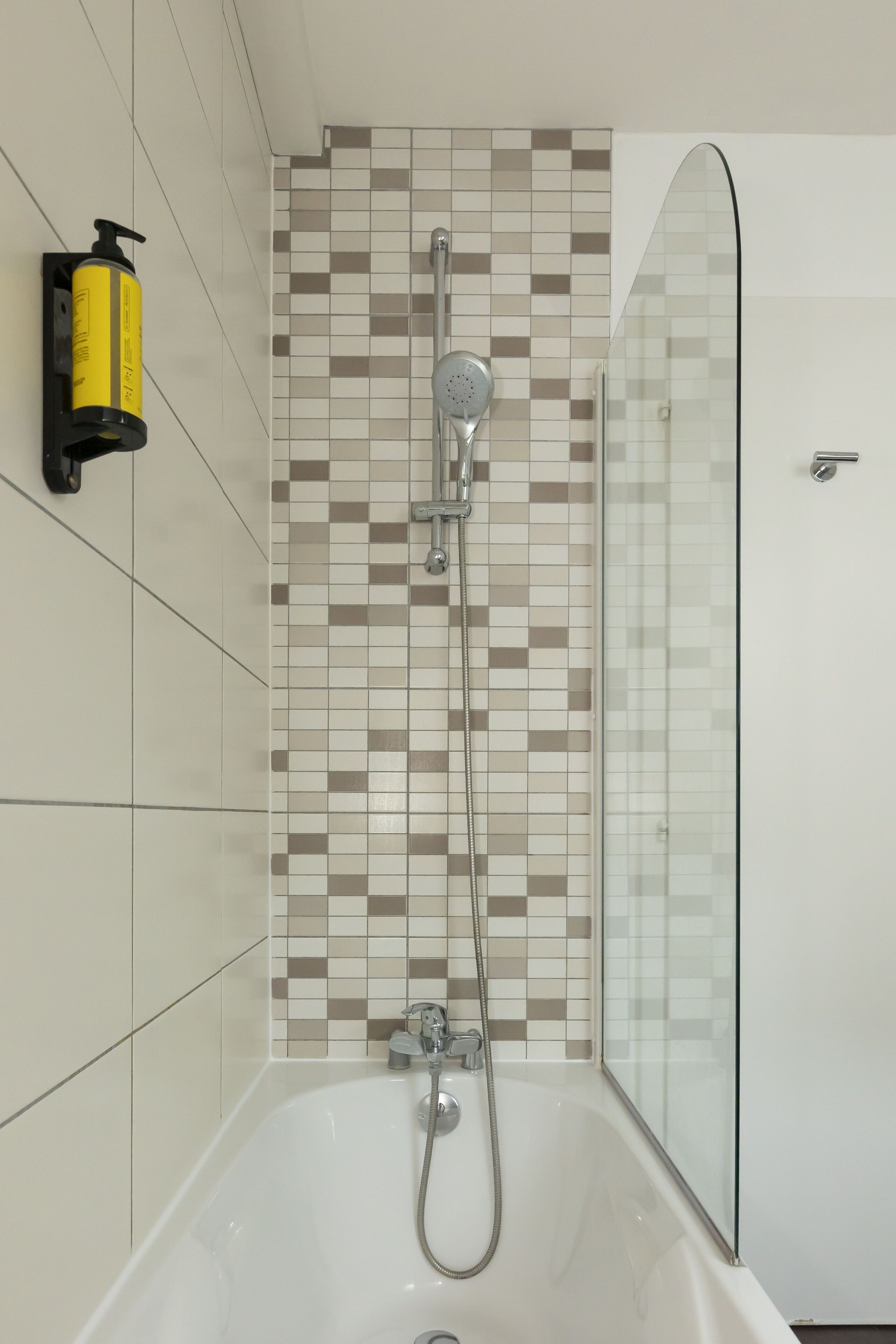 Un baño moderno con ducha envuelta en vidrio, cabezal de ducha de mano y dispensador de jabón de pared.
