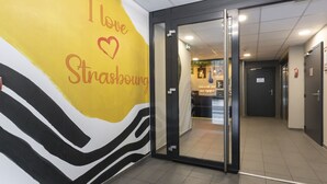 L’entrée d’un hôtel avec une porte en verre, un mur orné d’un motif à rayures et une enseigne sur laquelle on peut lire : « J’aime Strasbourg ».