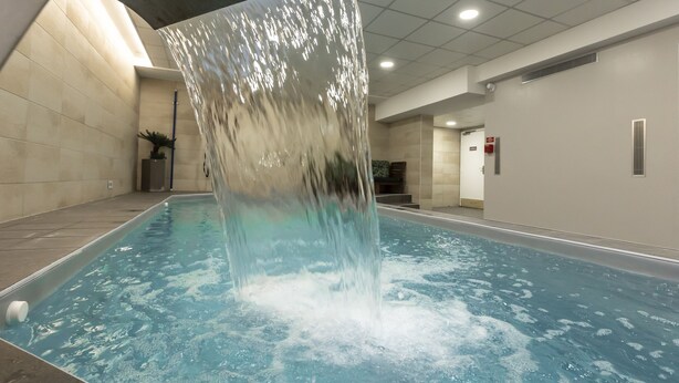 Une piscine intérieure agrémentée d’une cascade, avec des murs carrelés et une plante en pot.
