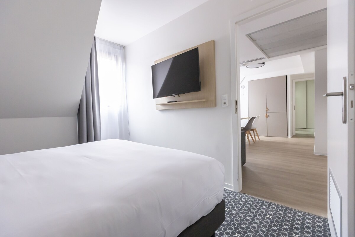 Une chambre d’hôtel avec un grand lit, un téléviseur fixé au mur et une vue sur la salle à manger.