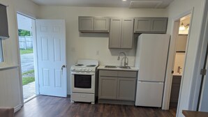 A compact kitchen with a stove, sink, and refrigerator, wooden flooring, and a door leading outside. - Regent Motel (Saint John)