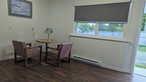 A room with a wooden floor, a round table with chairs, a lamp, a window with a roller blind, and a framed picture on the wall. - Regent Motel (Saint John)