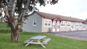 A motel with a picnic table in the front yard, a tree, and a parking lot. - Regent Motel (Saint John)