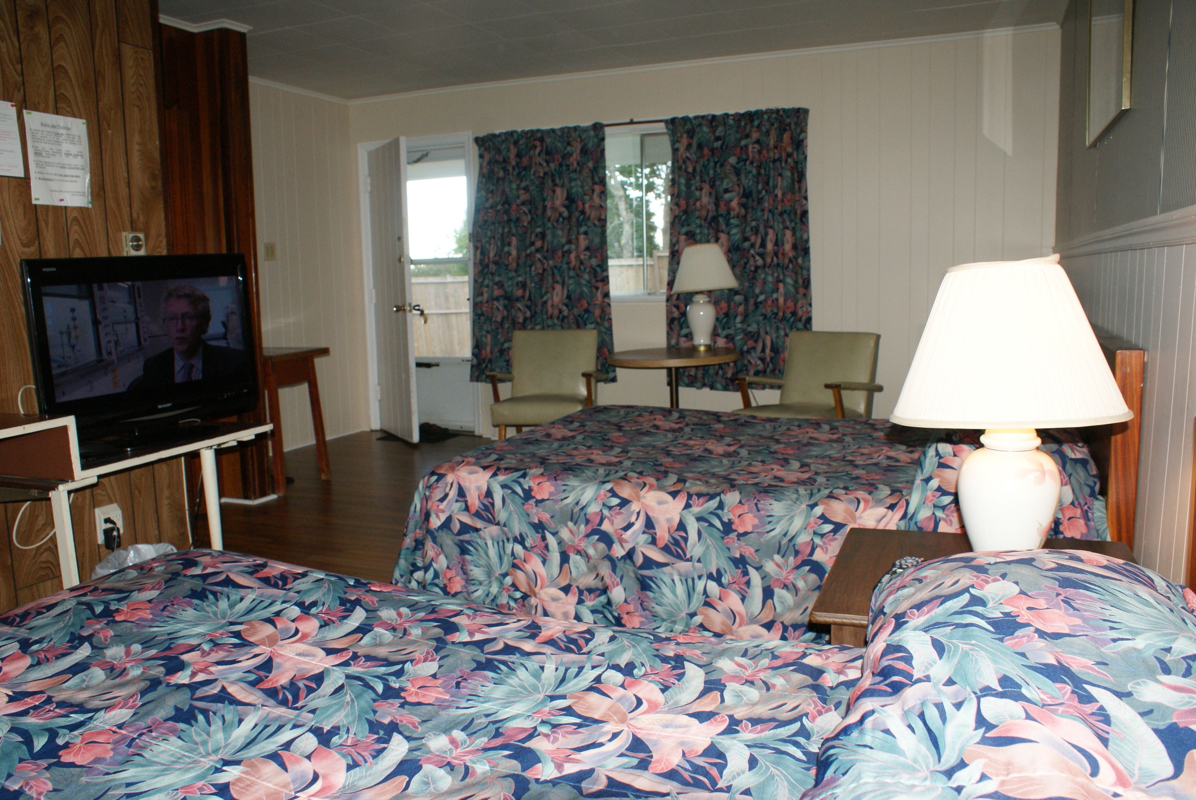Una habitación de hotel con dos camas, una televisión, un escritorio con lámpara y una silla.