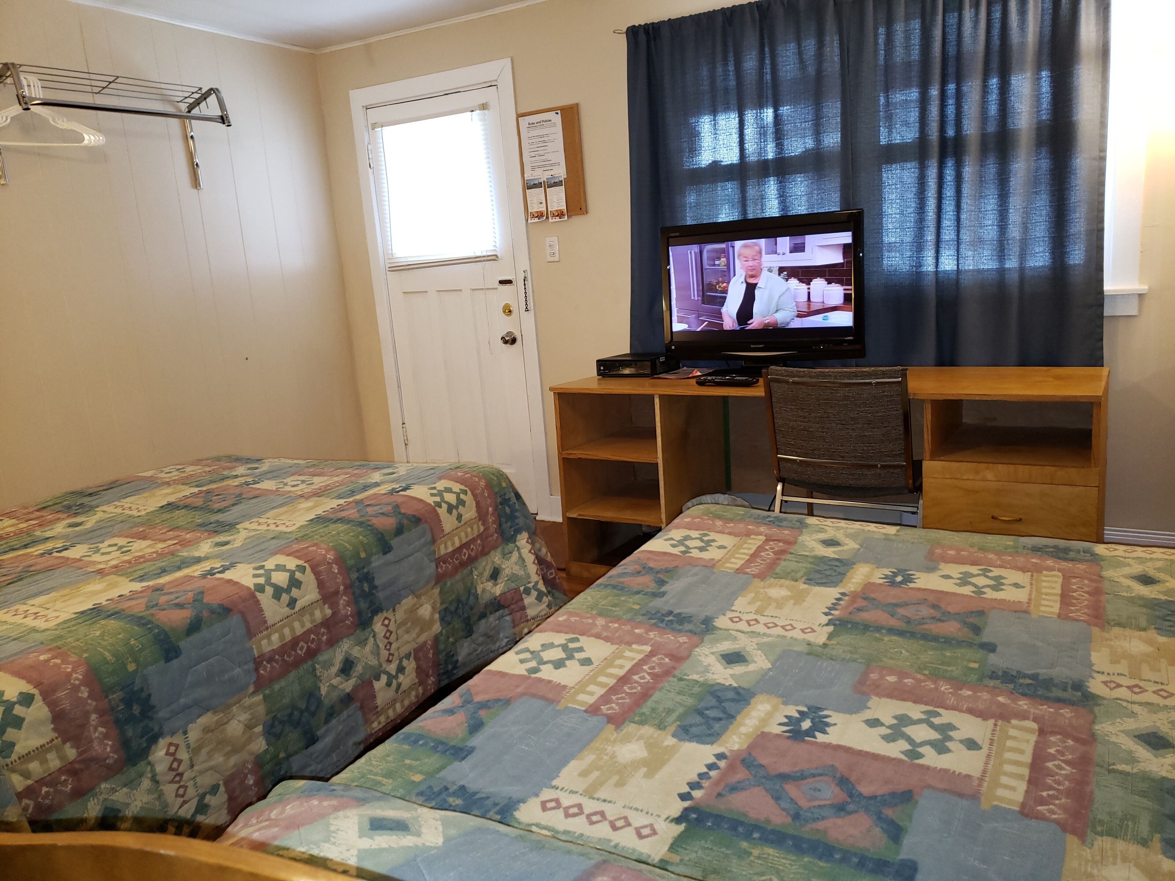 A room with two beds, a desk, a chair, a television, and a window with curtains.