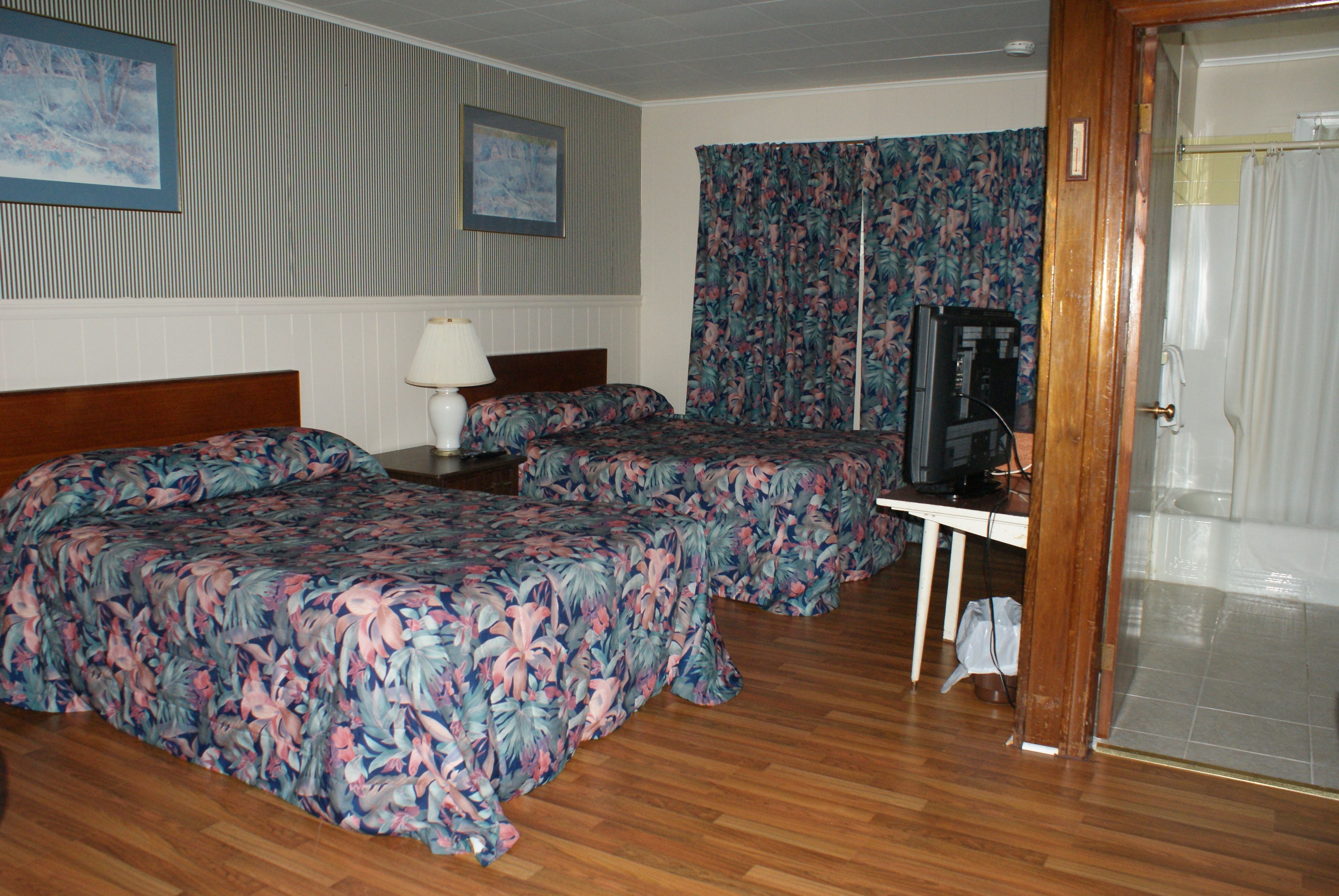 A hotel room with two beds, a desk, a television, and a shower area.