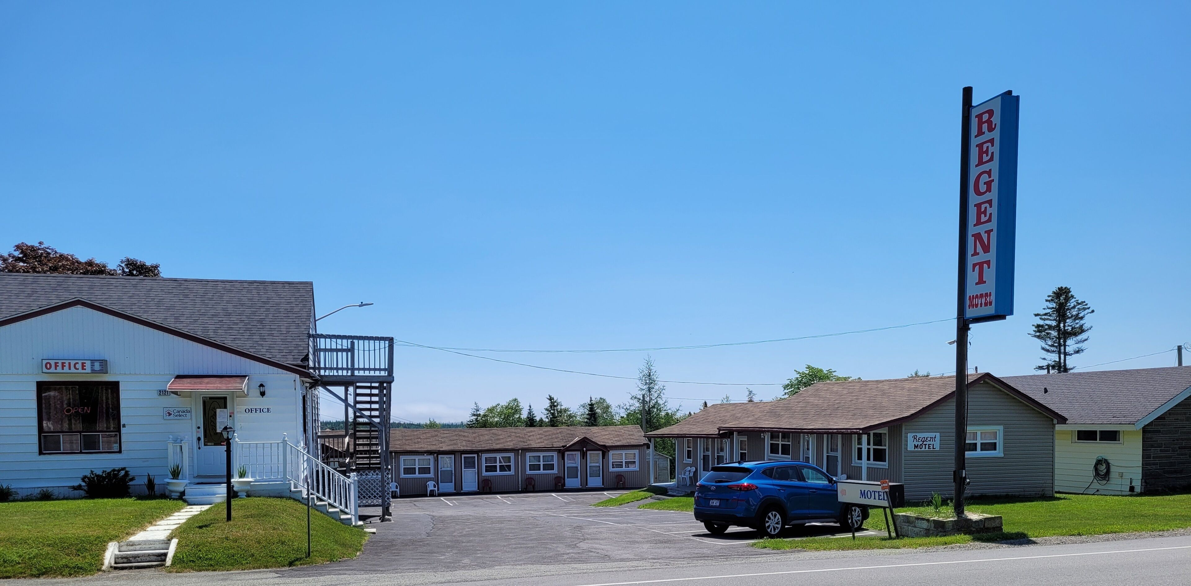 Un motel avec un panneau indicateur, un petit bureau et un espace de stationnement.