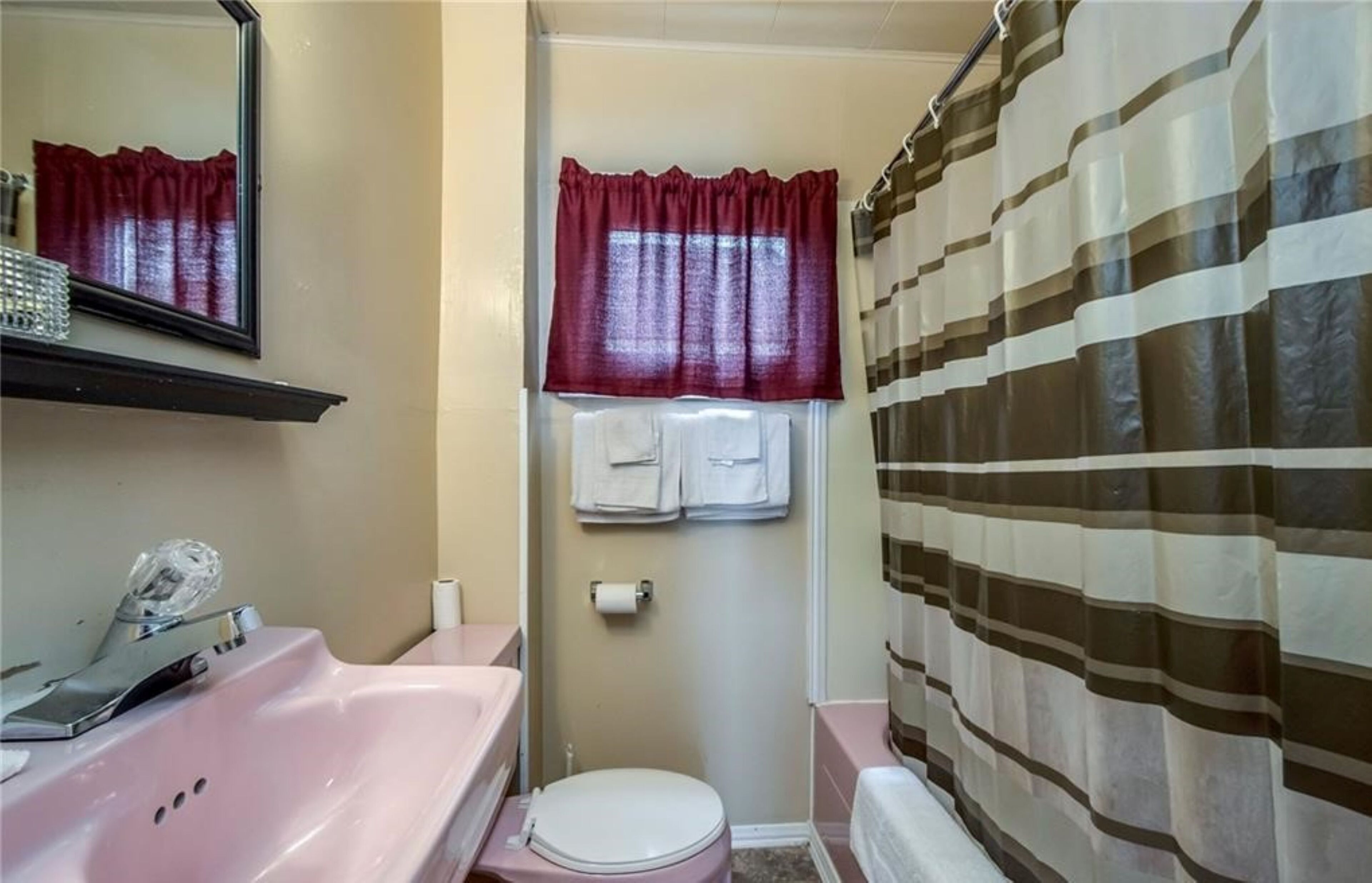 Un baño con lavabo rosa, espejo, inodoro y cortina de ducha a rayas.