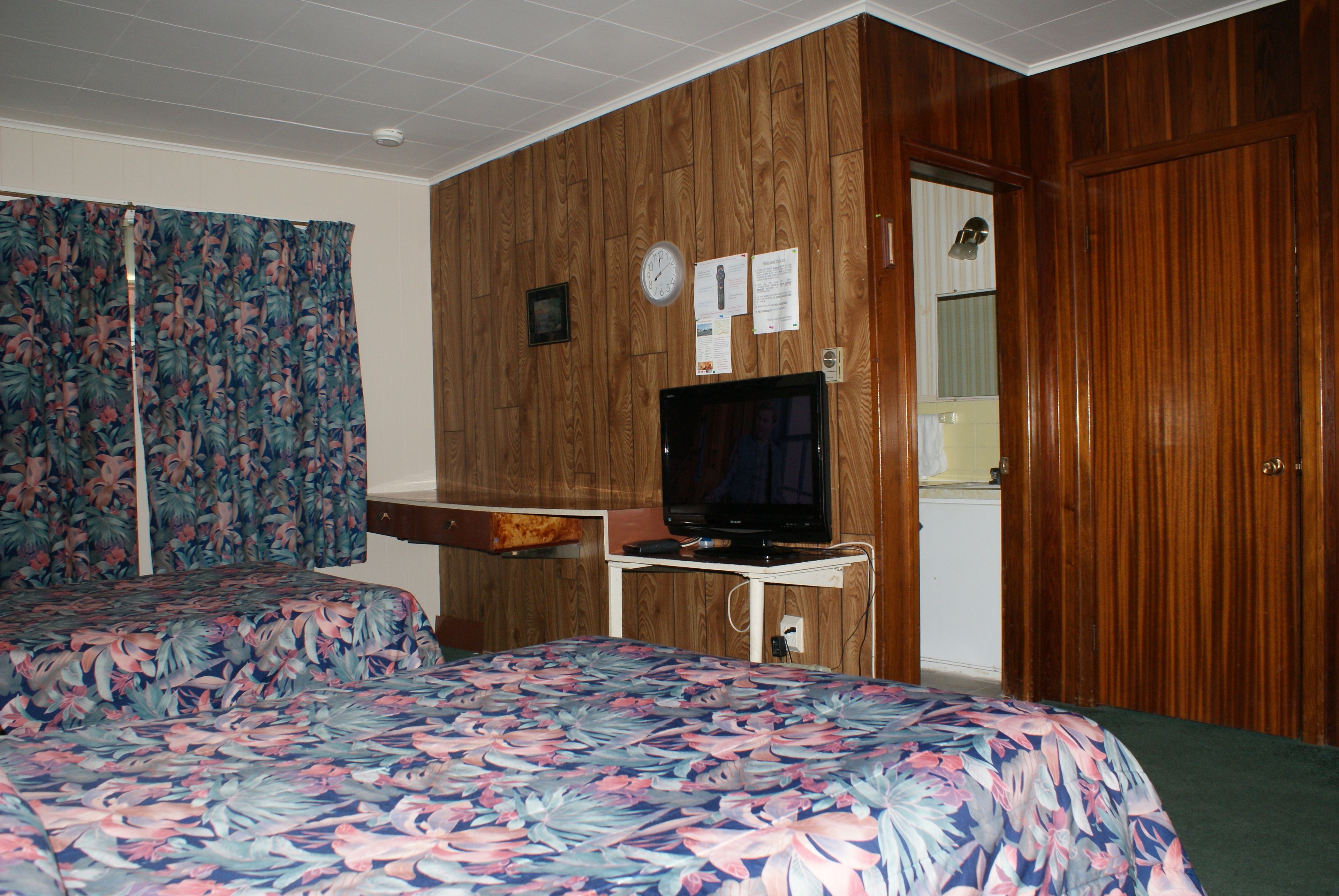 A room with two beds, a television, and wooden paneling.