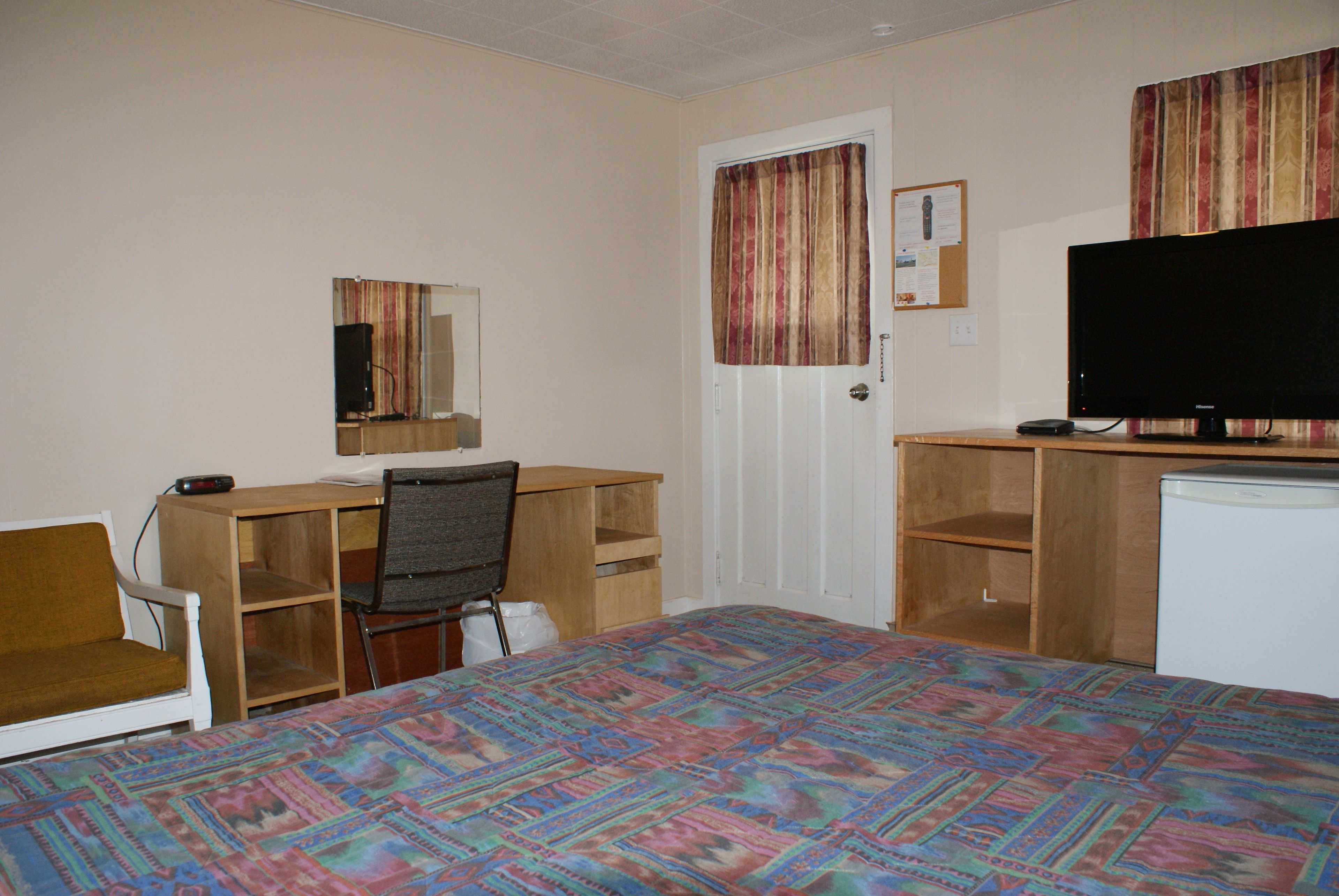 Een slaapkamer met een bed, een bureau, een stoel, een televisie en een kleine koelkast.
