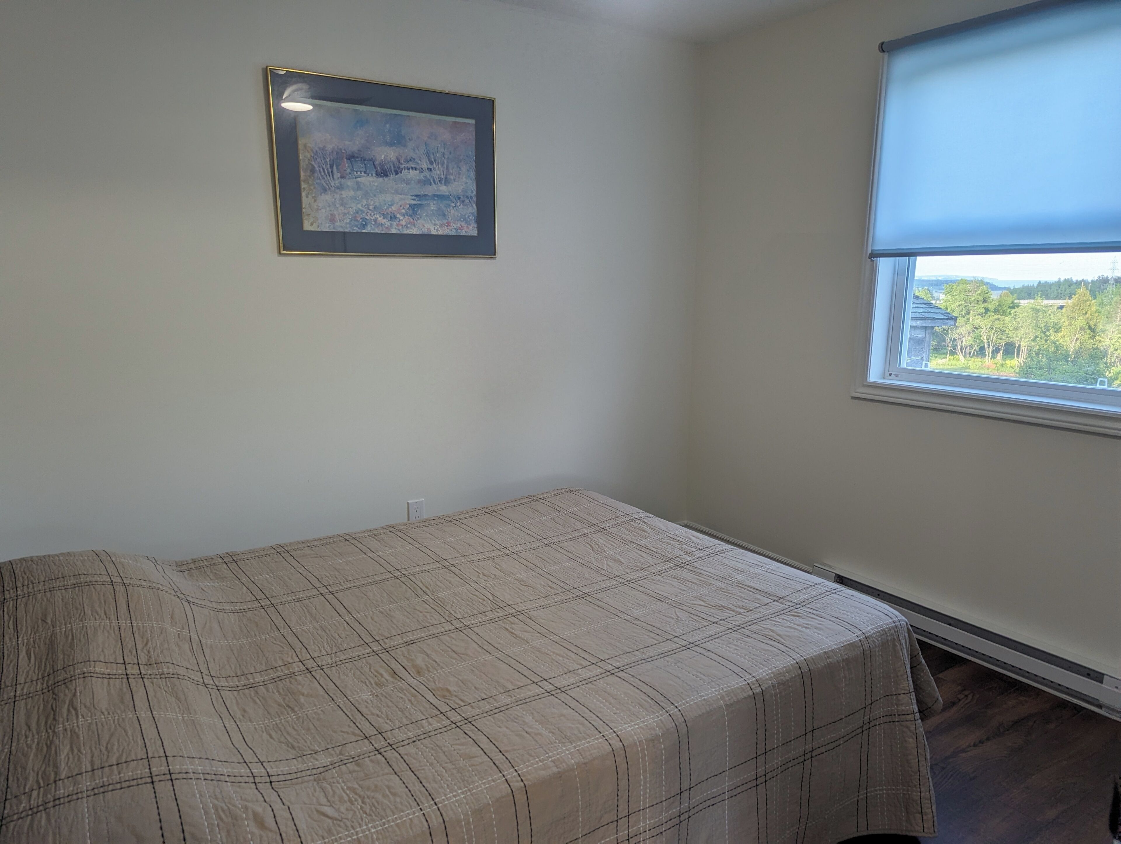 A room with a bed, a window with a view, and a framed picture on the wall.