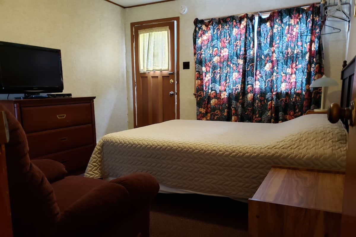 A bedroom with a bed, a dresser, a television, a door, and curtains.