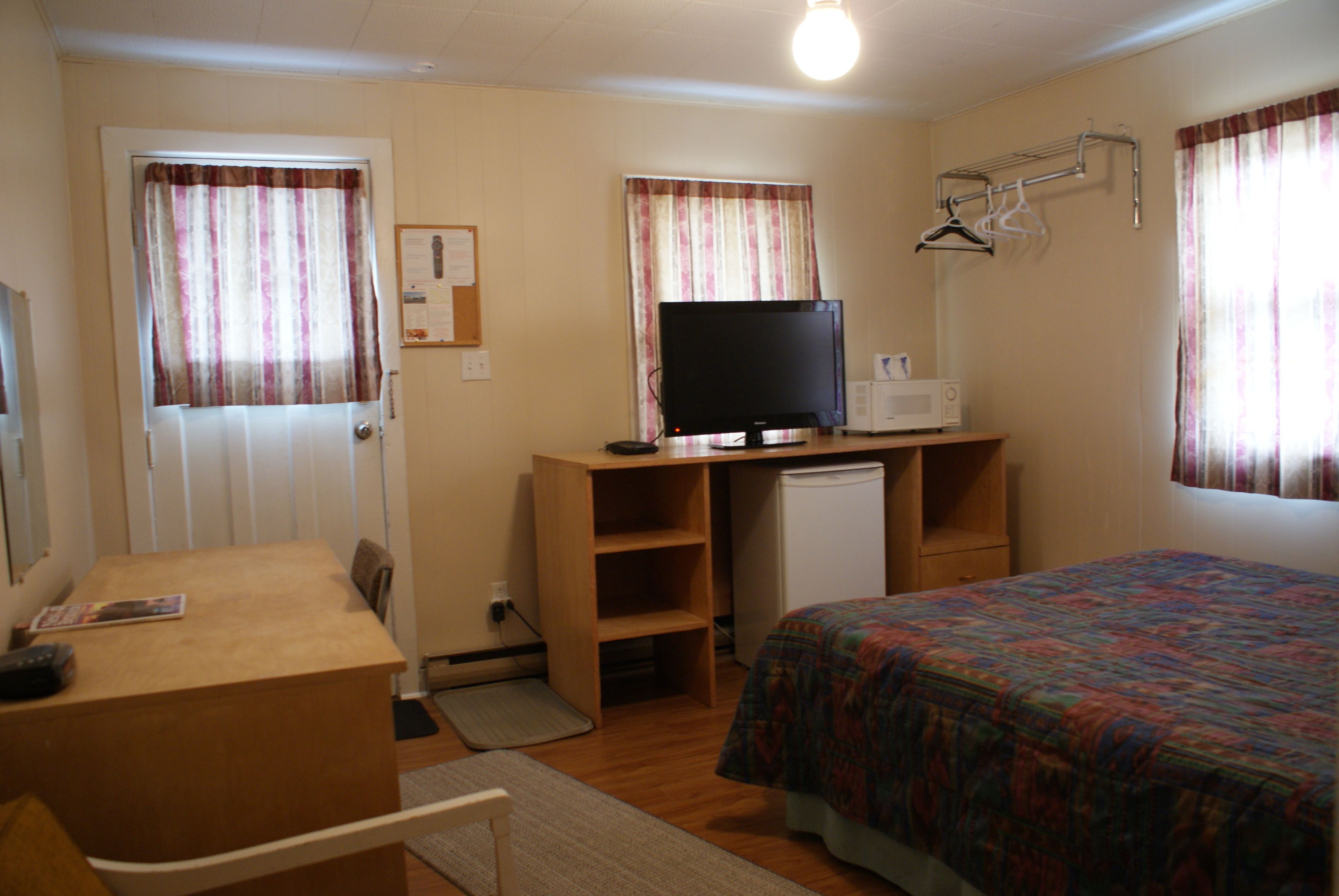 Un dormitorio con una cama, un escritorio con computadora, un microondas y un refrigerador pequeño.
