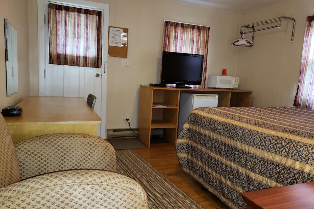 A hotel room with a bed, a desk with a television, a small refrigerator, and a chair.