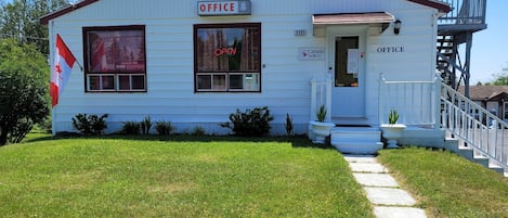 Un edificio bianco con una bandiera rossa, un cartello con la scritta 'OFFICE' e un'insegna 'APERTO' sulla finestra.