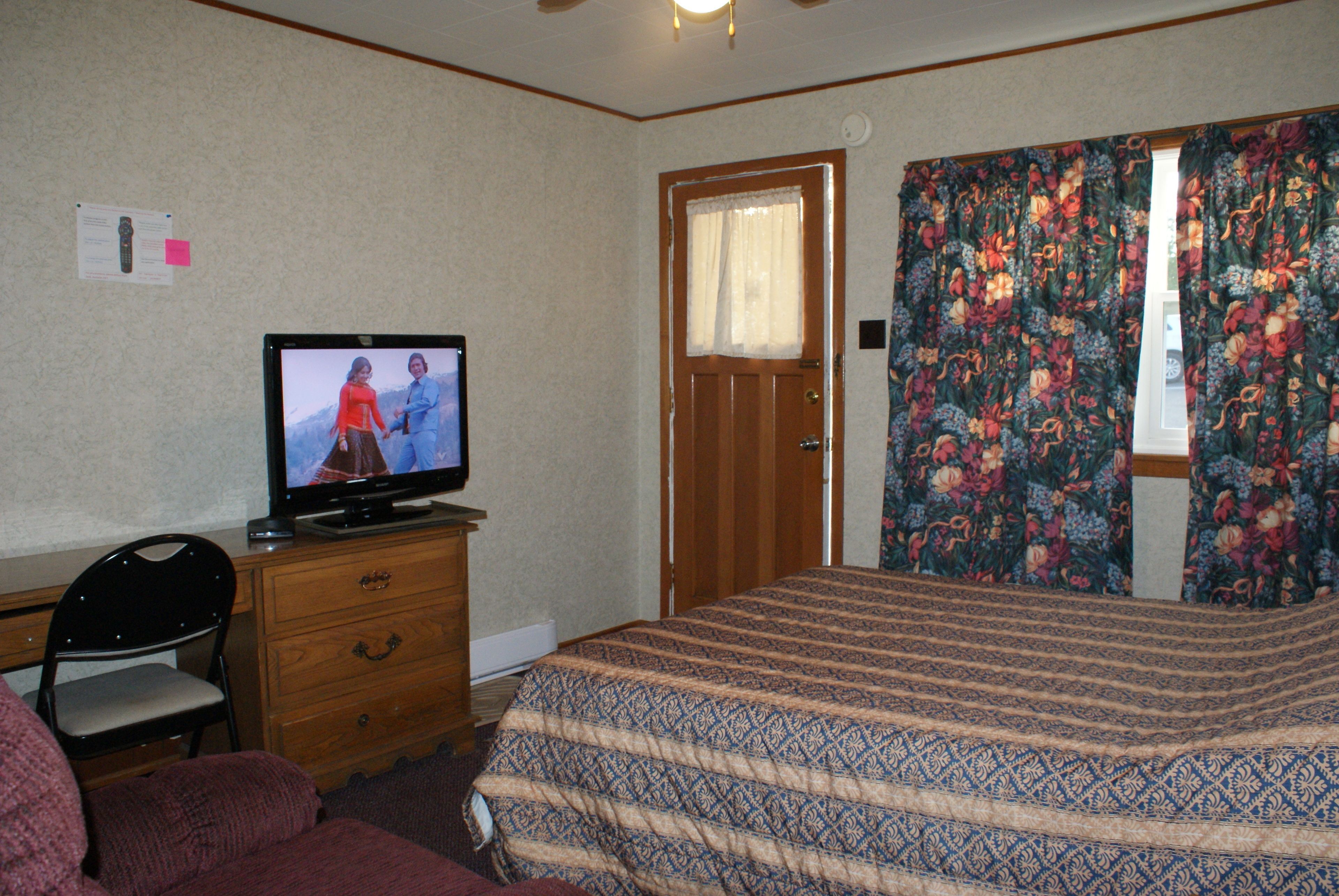 A bedroom with a bed, a television on a dresser, a chair, and a door.