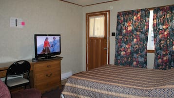 Un dormitorio con una cama, un televisor sobre una cómoda, una silla y una puerta.
