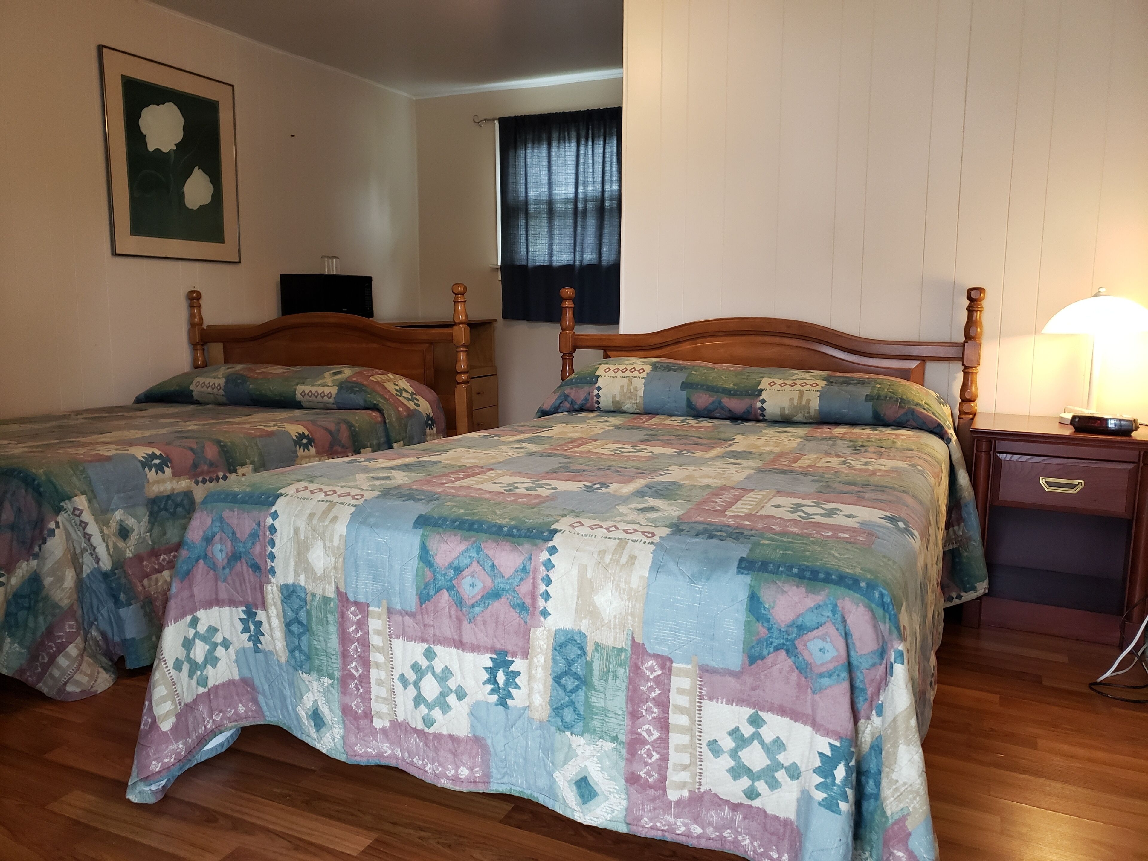 Une chambre à coucher avec deux lits en bois, une table de chevet, une lampe et une fenêtre avec des rideaux.