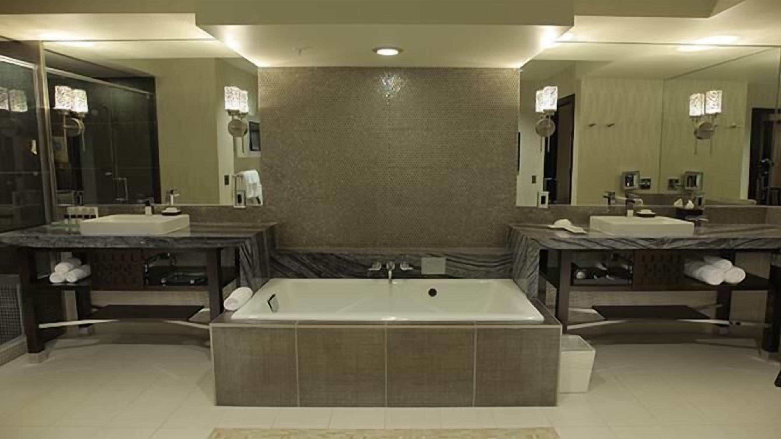 Un bagno moderno con una grande vasca da bagno al centro, due lavabi e un ampio specchio.