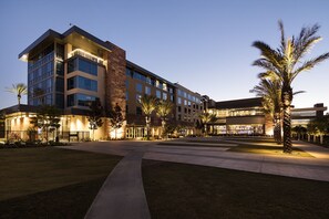 A multi-story hotel with a modern design, featuring a central courtyard with palm trees and a well-lit entrance.