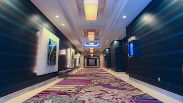Pasillo de hotel con alfombra estampada, paredes oscuras y un letrero que indica la dirección a los ascensores.