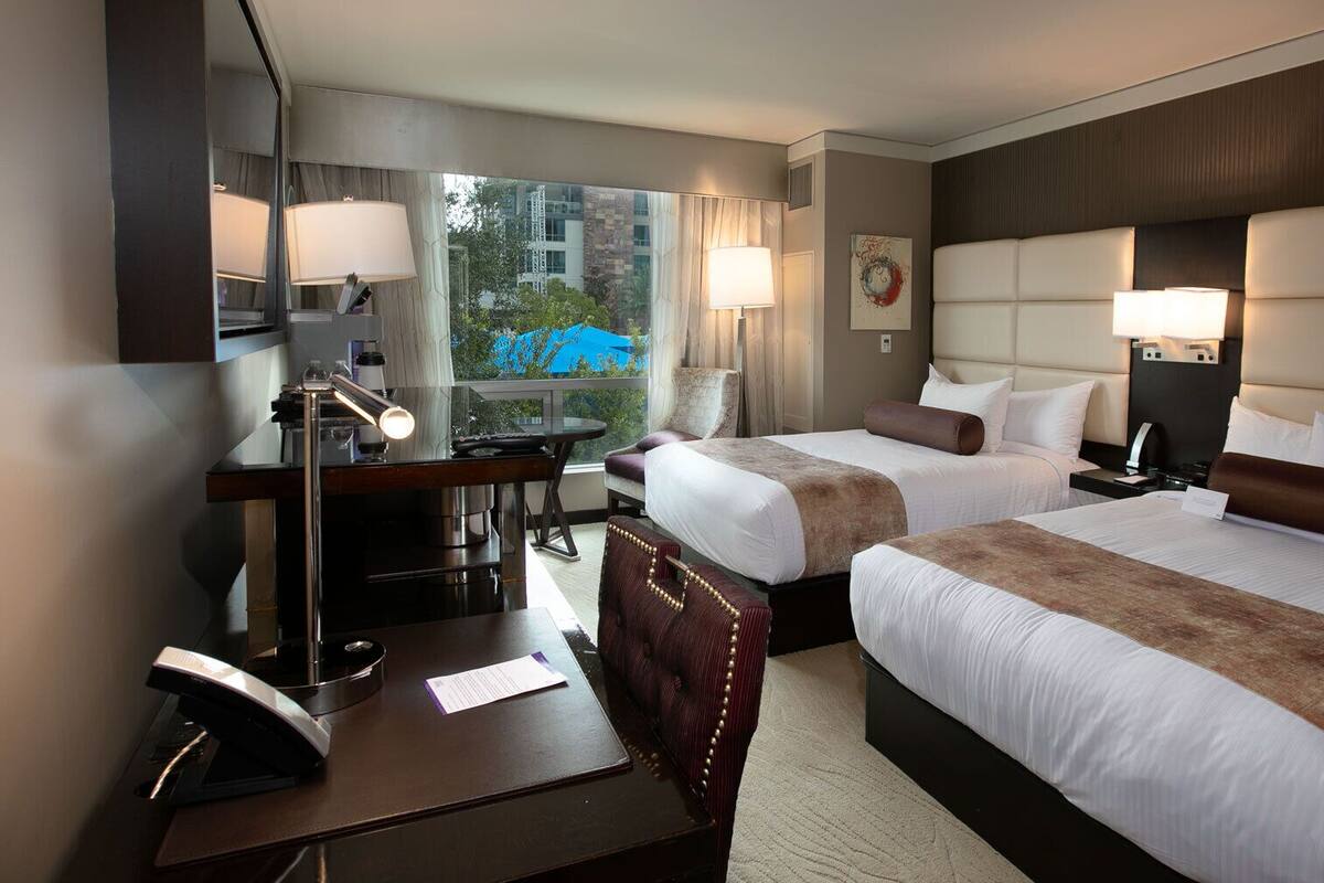 Une chambre d’hôtel avec deux lits, un bureau, une chaise et une lampe de bureau.