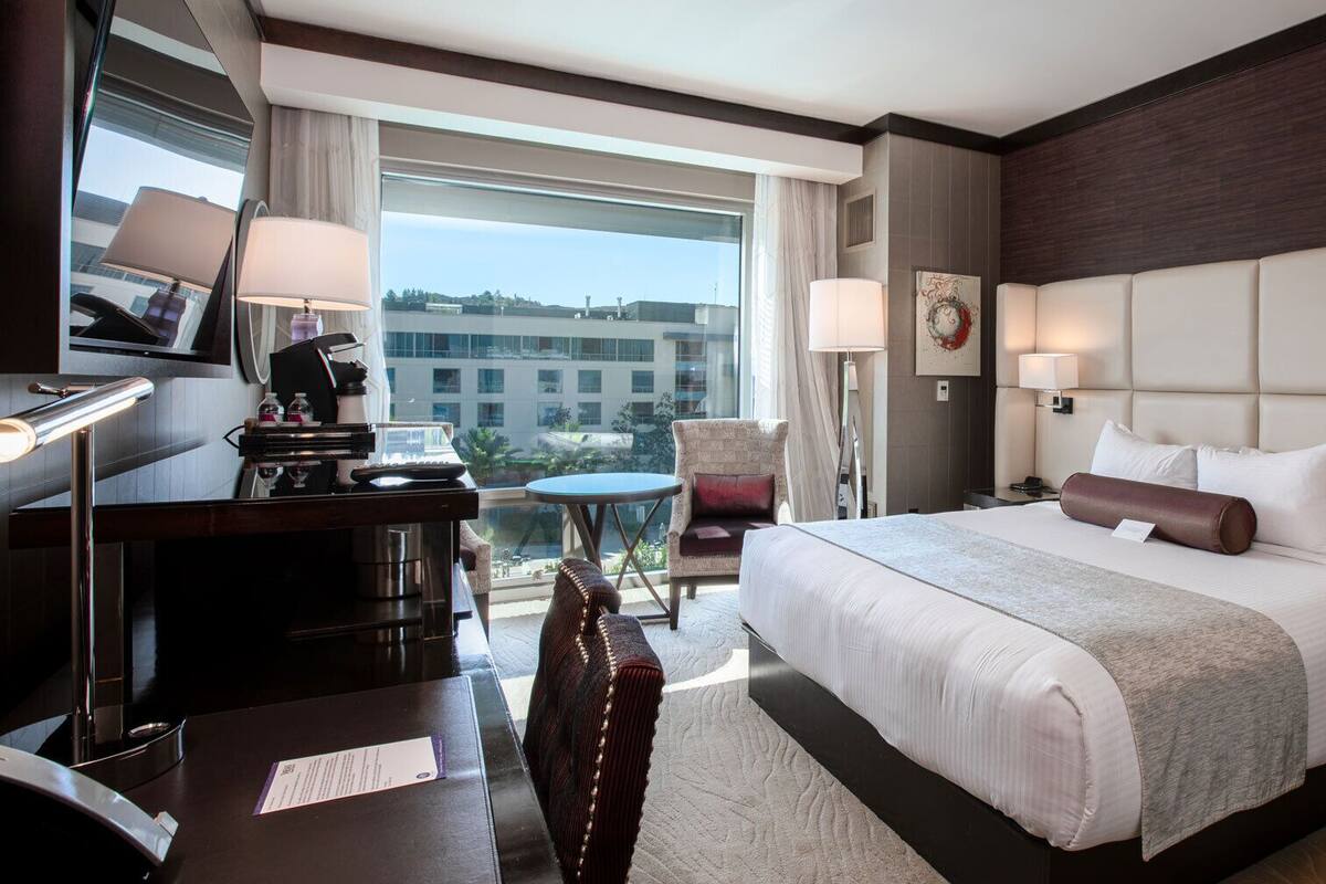 Une chambre d’hôtel avec un grand lit, un bureau avec une lampe, une chaise et une vue sur la ville.