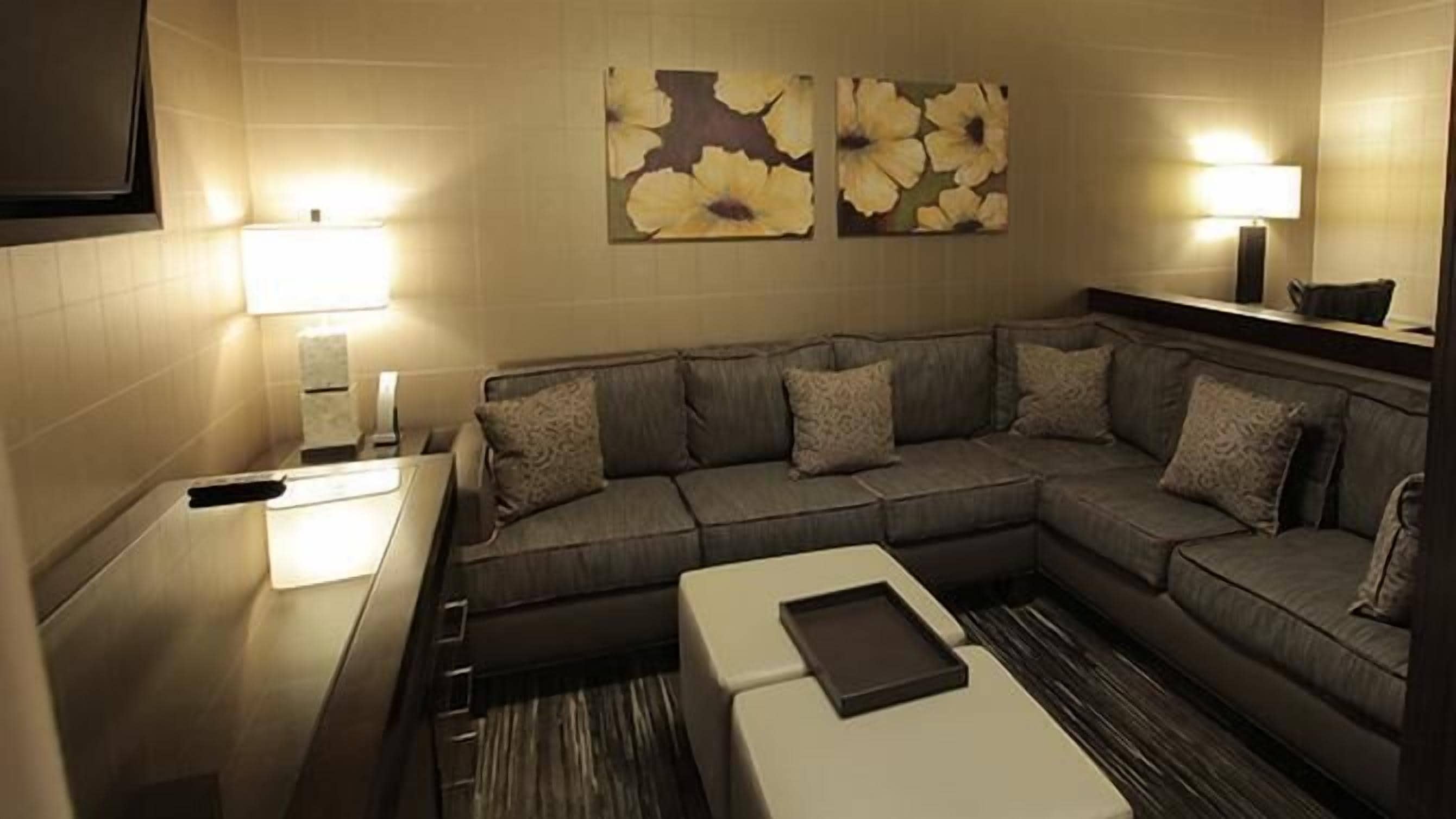 A modern hotel room with a sectional sofa, a small table, and two wall-mounted lamps.
