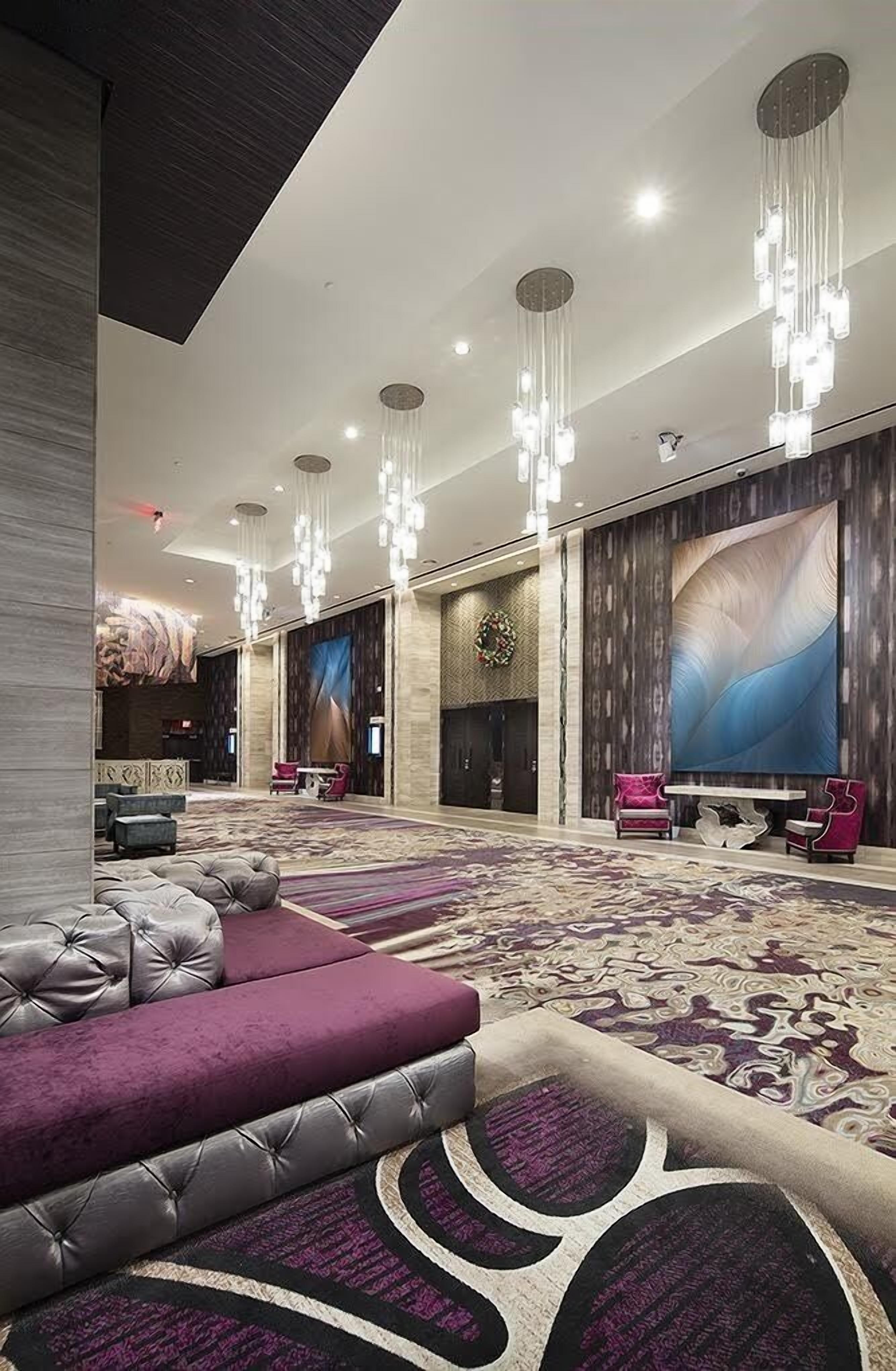 A spacious lobby with a large seating area, a high ceiling with hanging lights, and a large abstract painting on the wall.