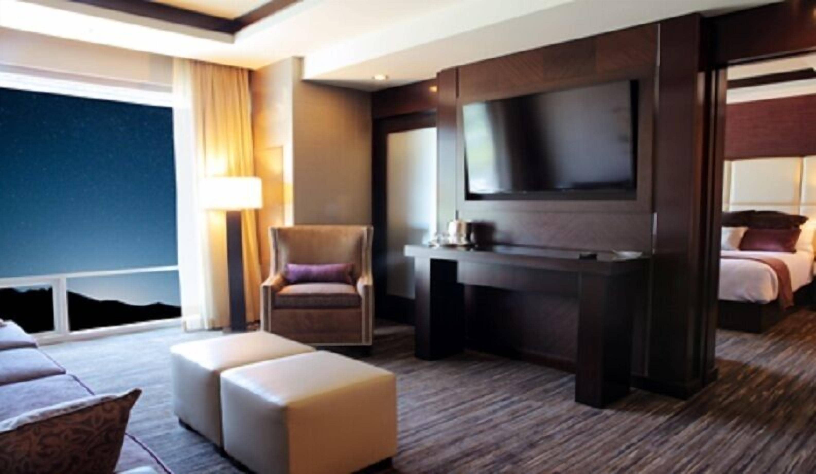 Una habitación de hotel moderna con un televisor de pantalla plana grande, un sofá cómodo, una silla y una cama con cabecero.