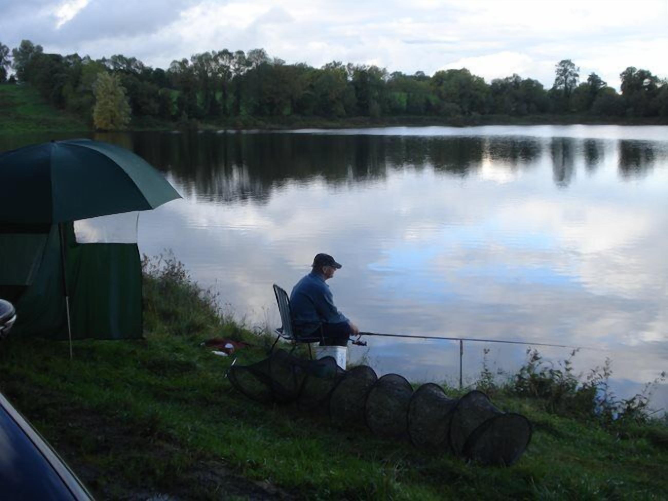 A person fishing by a calm lake with a tent nearby.