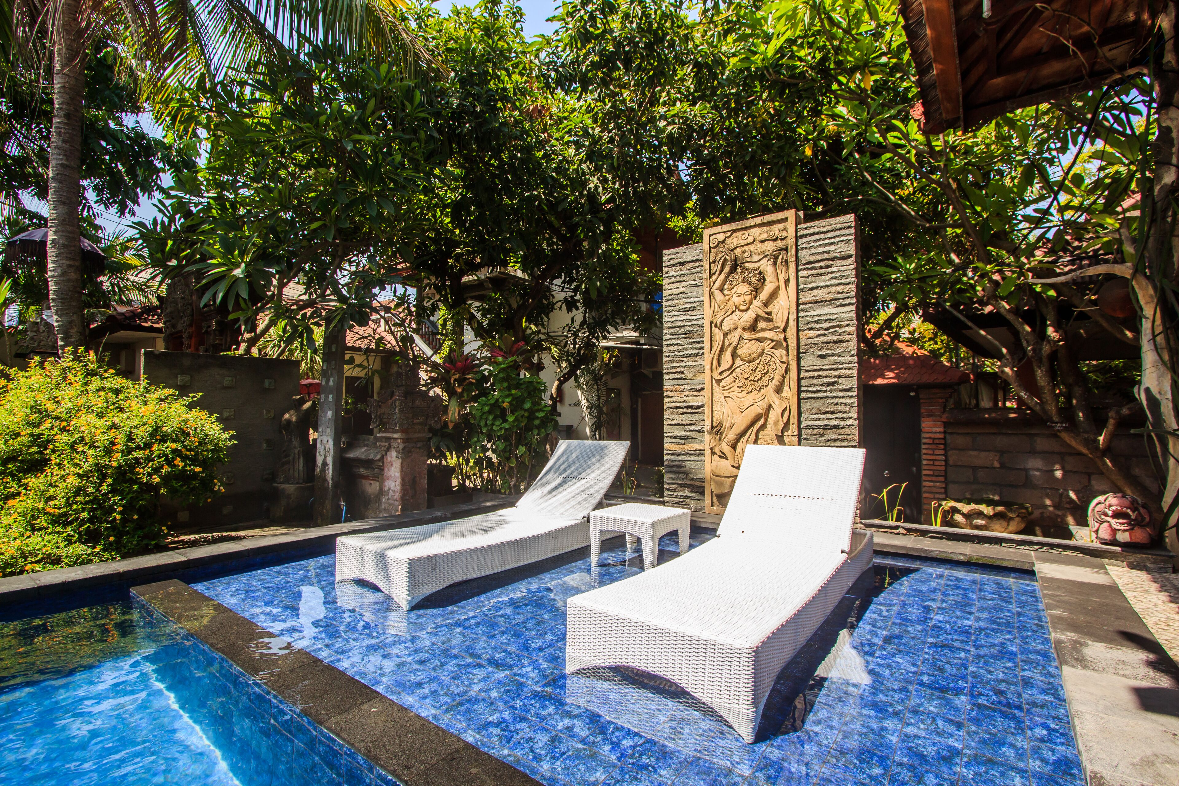 A swimming pool with two white lounge chairs and a stone wall with a relief sculpture.