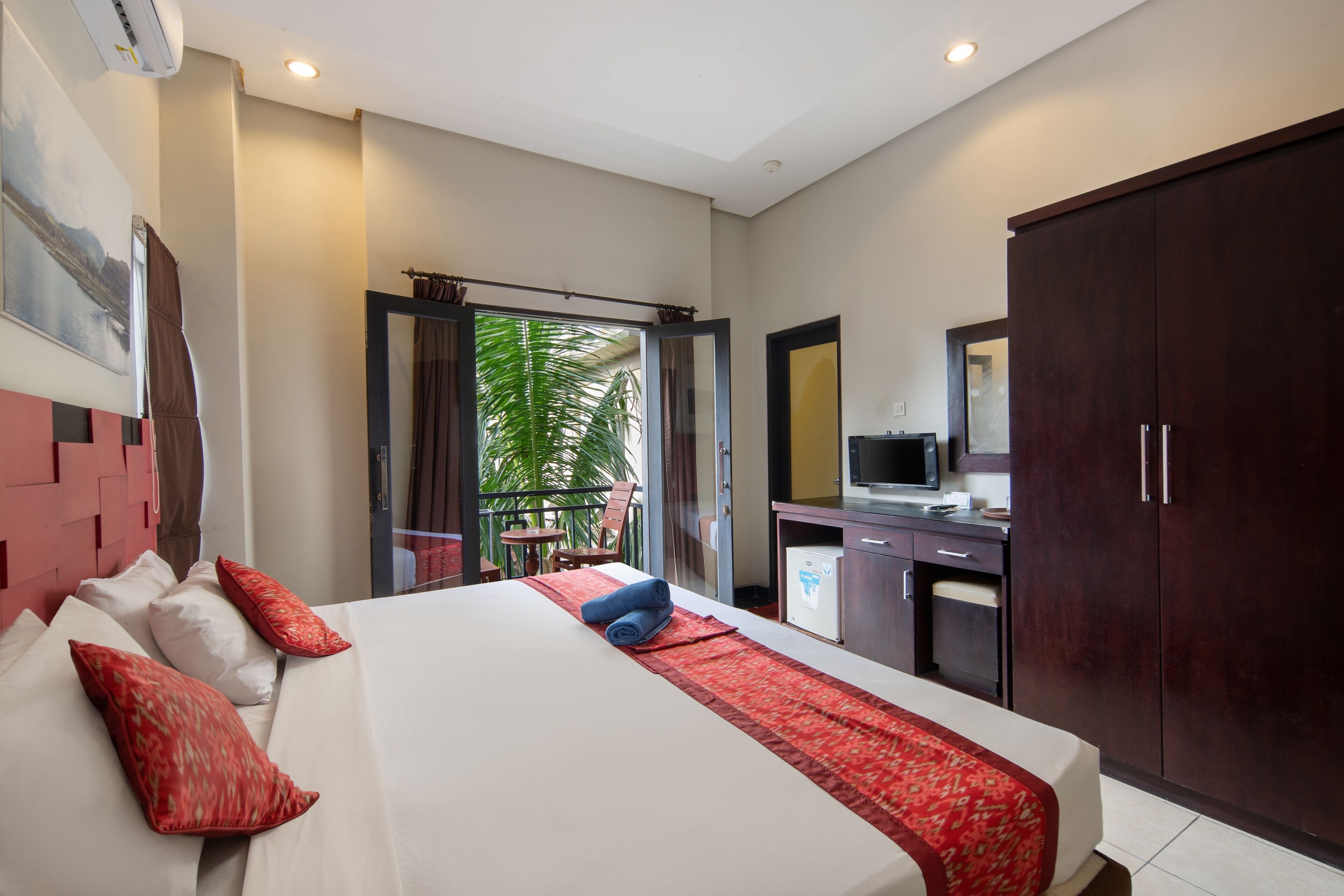 Una habitación de hotel con cama, escritorio, armario y balcón con vistas.