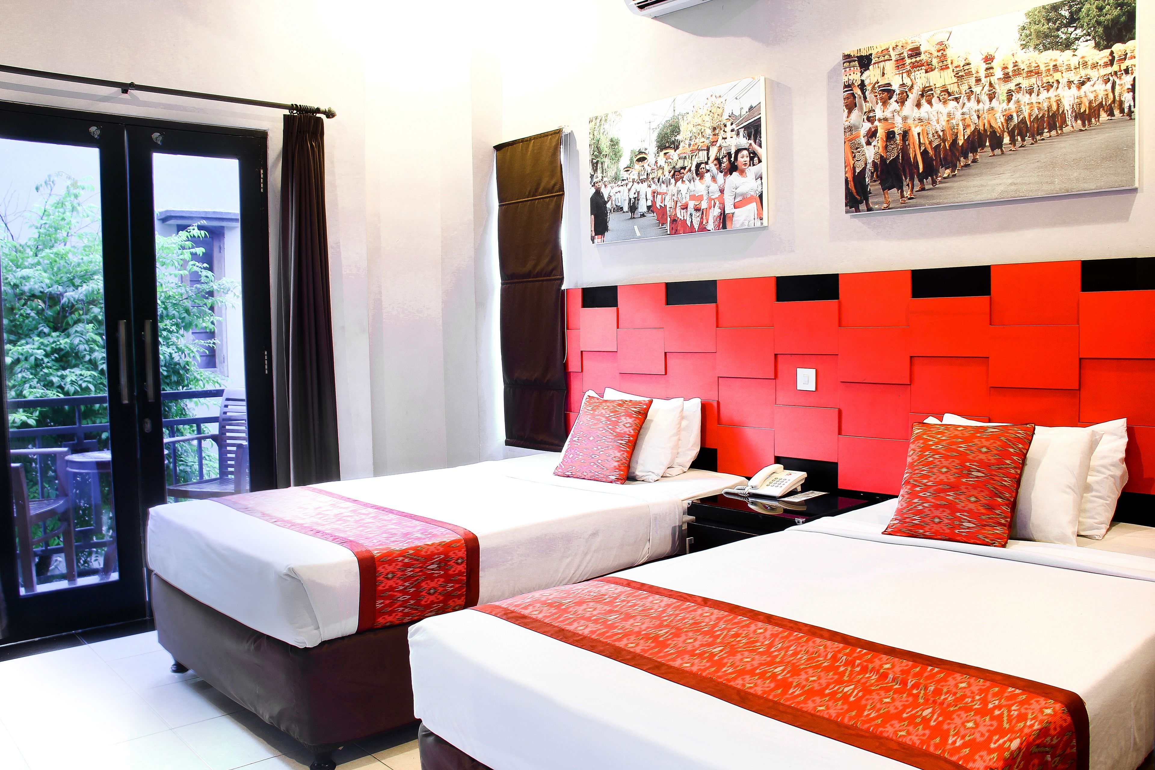 Une chambre d’hôtel avec deux lits, un balcon et un mur d’accent rouge.
