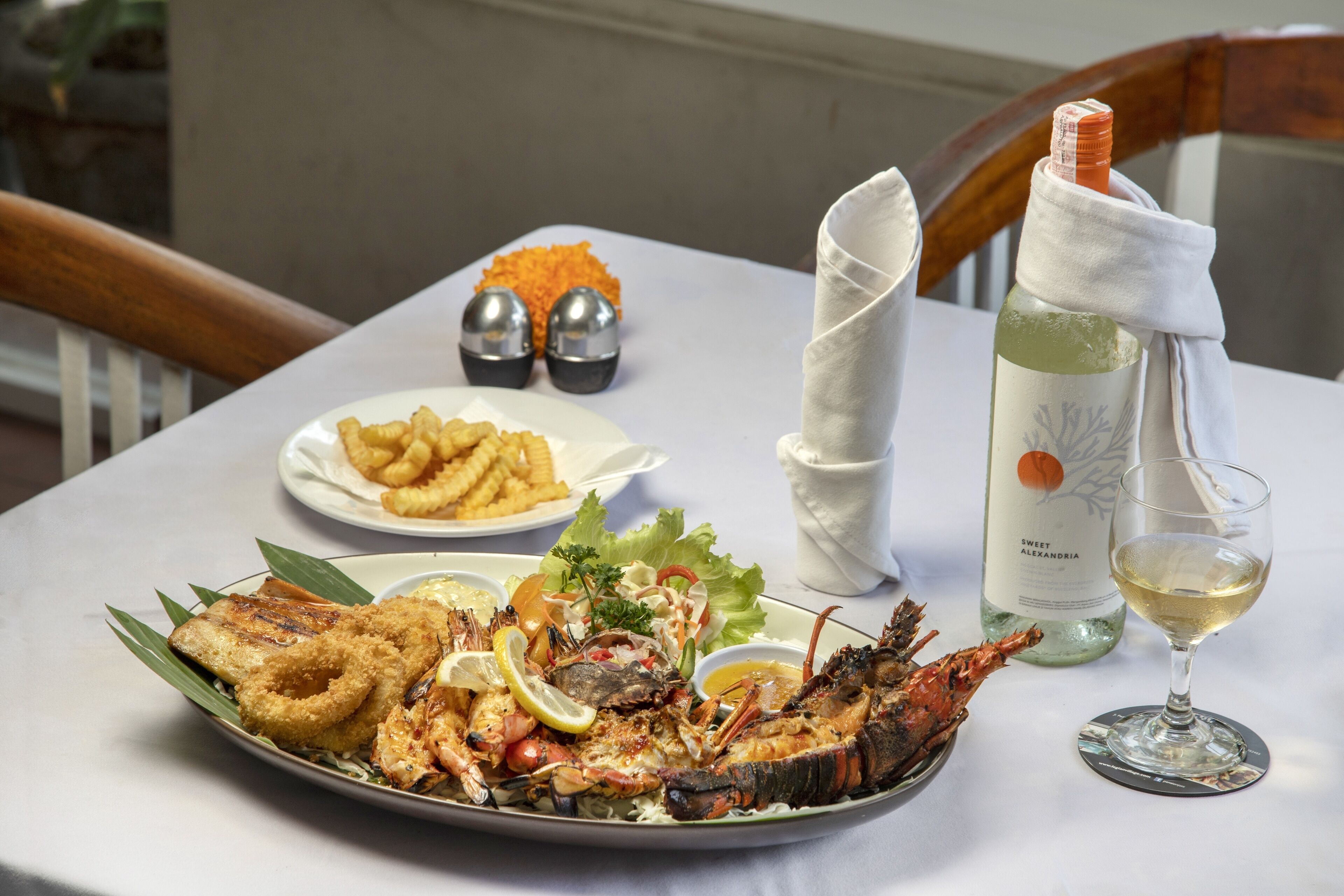 Una bandeja de mariscos con preparaciones fritas, ensalada y una botella de vino sobre una mesa.