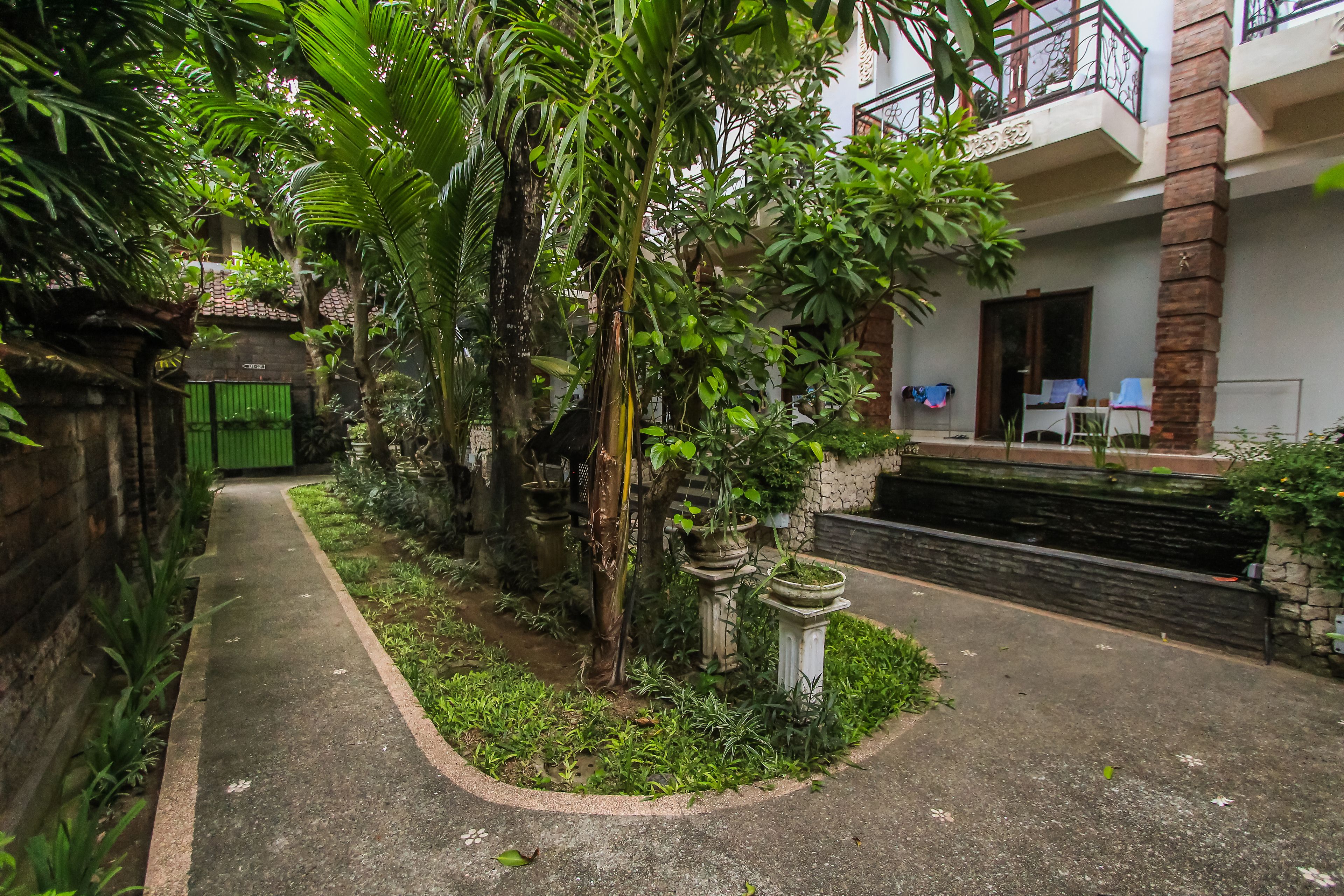 A courtyard with a concrete path, potted plants, and a building with a balcony.