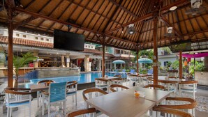 A poolside area with wooden tables and chairs, a bar, and a television screen. - Legian Village Hotel (Legian)