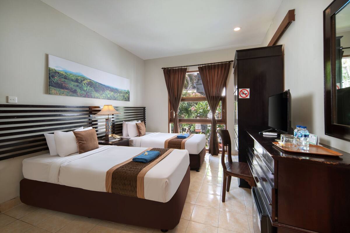 A hotel room with two beds, a desk with a TV, a chair, and a window with curtains.