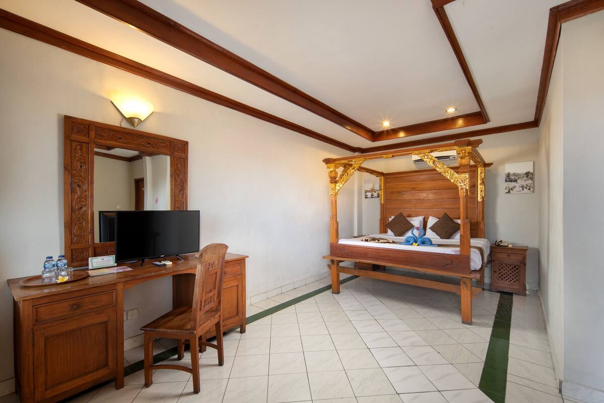A bedroom with a wooden bed, a desk with a television, a chair, and a mirror.