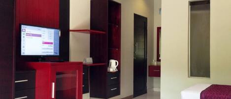 A hotel room with a TV, a coffee machine, a wardrobe, and a bed.