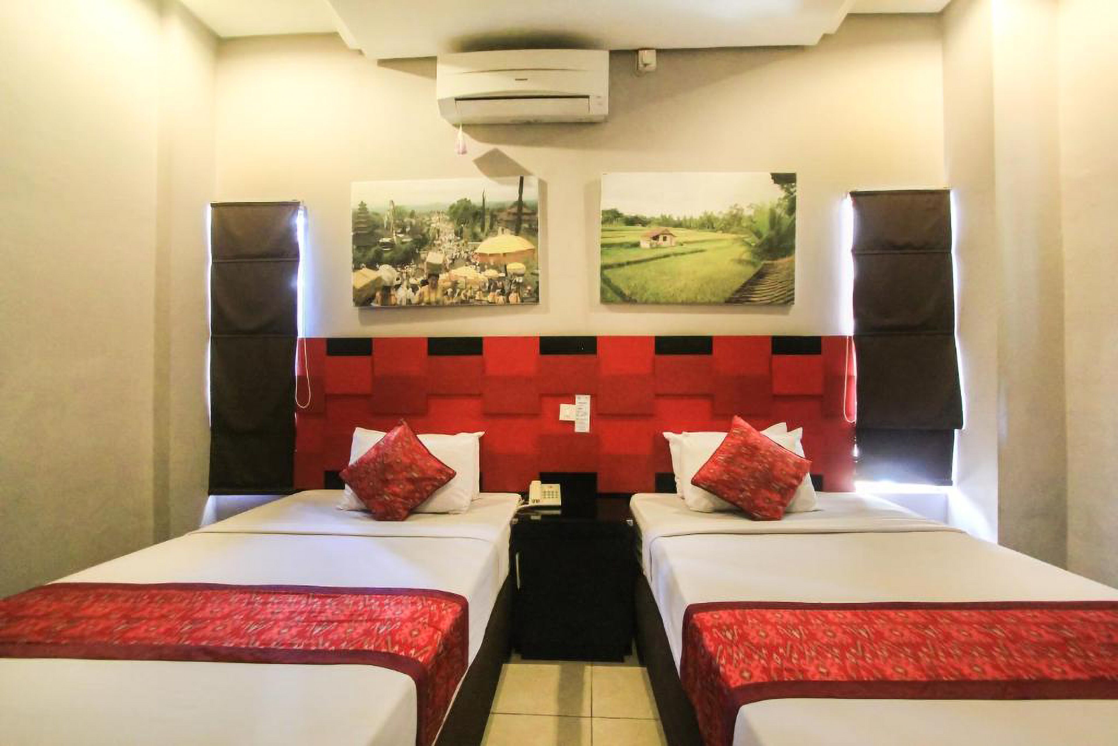 A hotel room with two beds, a red and black headboard, and two wall-mounted speakers.