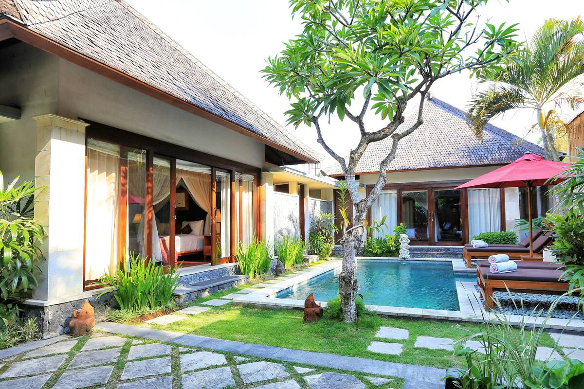 Una villa con piscina privada, zona de estar exterior cubierta y jardín con sendero de piedra.
