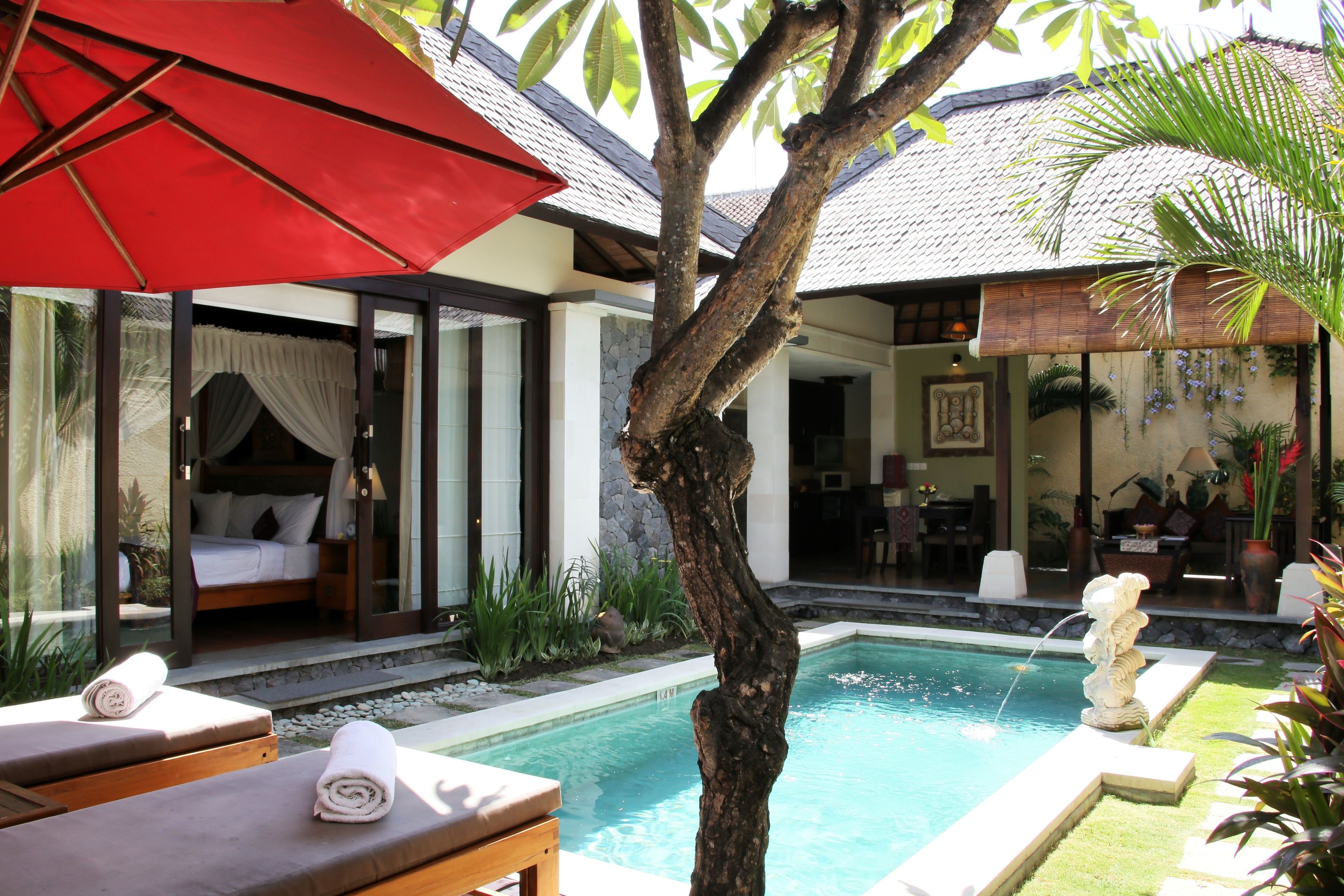 A poolside area with a bed, lounge chairs, and a red umbrella.