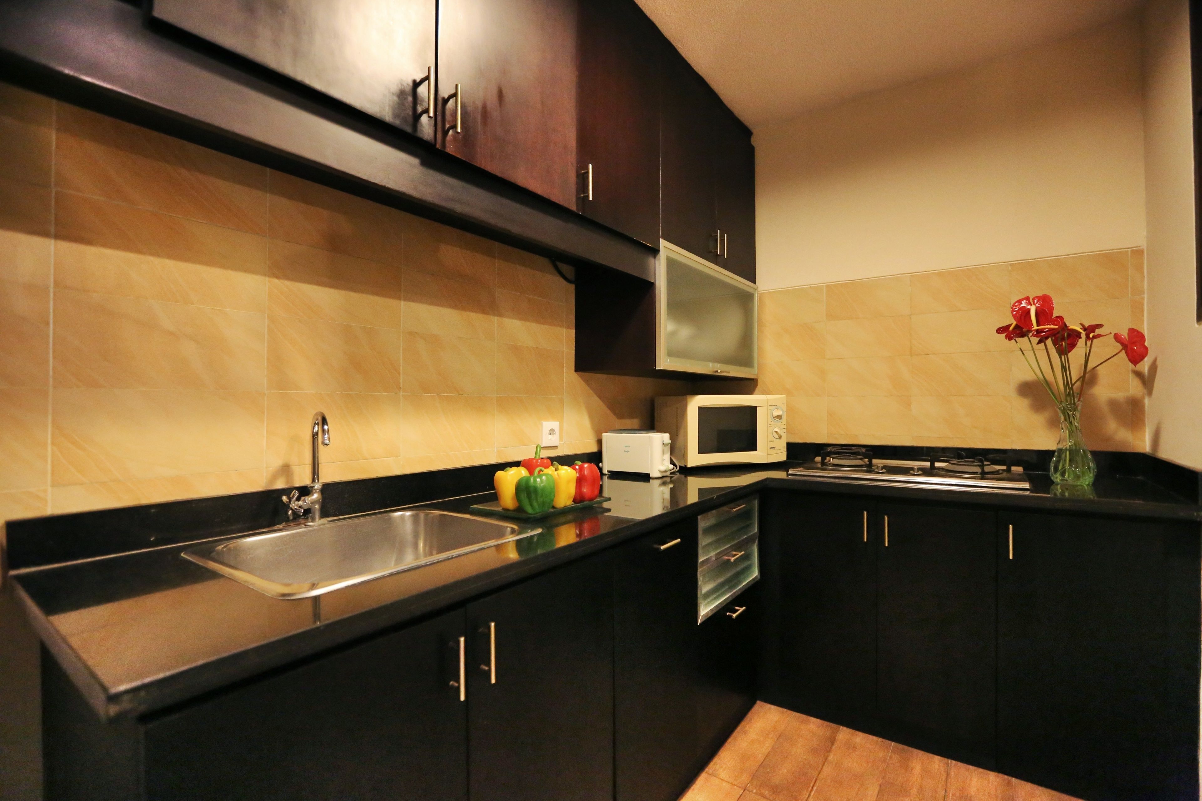 A modern kitchen with dark cabinets, a stainless steel sink, a microwave, and a stove.