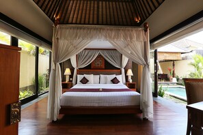 Una cama con dosel y cuatro columnas con ropa de cama blanca, cabecera de madera y dos mesitas de noche con lámparas.