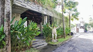 A building with a stone facade, a statue, and lush greenery including palm trees and large leafy plants. - Akarsa Kokoro Sanur Bali (Denpasar)