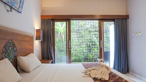 A hotel room with a large bed, a wooden headboard, a view of greenery through a sliding door, and a decorative wall piece. - Akarsa Kokoro Sanur Bali (Denpasar)