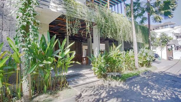 A building with a covered outdoor area, surrounded by various plants and palm trees. - Akarsa Kokoro Sanur Bali (Denpasar)