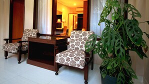 A room with two patterned armchairs, a small wooden table, and a large potted plant. - Jesens Inn 2 (Kuta)